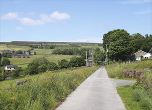 Narrow country lane with the village of wadworth and hillside fields near hebden bridge in