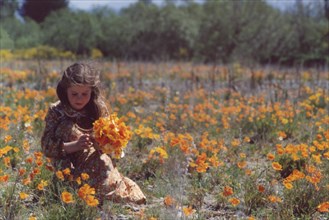 Girl in floral dress picking yellow flowers in dry river bed