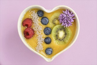 Peach smoothie bowl with blueberries, kiwi, white chia seeds and raspberries in a heart shaped bowl