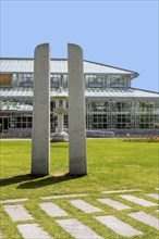 Modern architectural glass building with central stone sculpture, amid a green park setting and