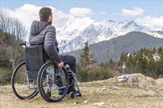 Photo of Young disabled man in wheelchair outside in nature observing mountains and nature