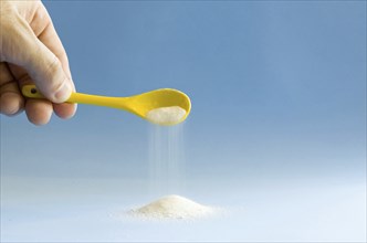 Yellow spoon turning sugar on blue background