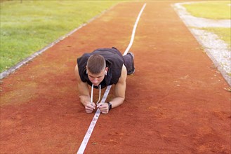 Young man doing plank exercise in the morning outdoor on the running race track