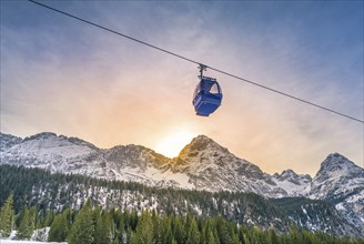 Cable car route going over the Austrian alps mountains with their fir forests, while the sun sets