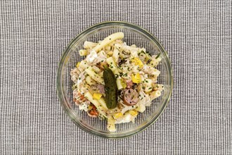 Pasta salad dish with corn, tuna and a pickle on a gray background