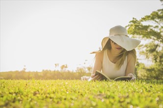 Pretty woman reading book lying on the lawn, seen from above with summer hat