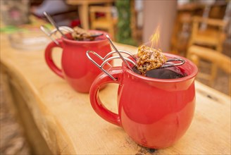 Image with a mug of hot wine, which has tongs with a flaming cone of sugar on top. It is a