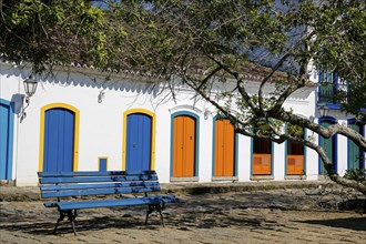 View to colonial house facades with colorful wooden doors in sunshine with a blue bench and tree