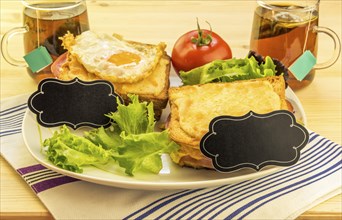 Plate with sandwiches, fried egg, tomato and green salad on wooden table. Each sandwich has a blank