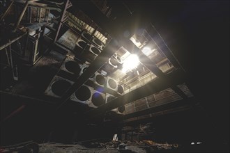 A dark interior of an industrial plant with rays of light shining through the roof, Metallwerke