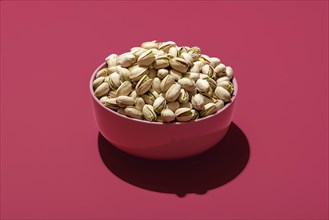 Pink bowl with roasted and salted pistachio minimalist on a magenta table. Bowl with pistachio