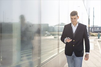 Young and Casual Businessman Using Smartphone while Walking Outside of Office Building