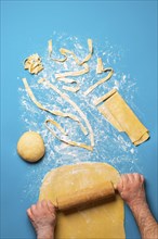 Man rolling semolina dough to make pasta, on a blue background. Top view of making tagliatelle