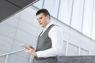 Young and Casual Businessman Using Tablet while Walking Outside of Office Building