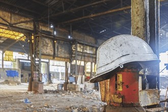 An abandoned construction helmet hangs from a metal post in a dilapidated warehouse, Metallwerke