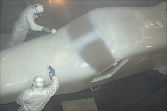 Tradesmen sprays top coat on the top of the nose on a Dornier 228 aircraft