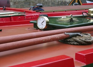 A close up of a brass gauge porthole boathooks and ropes on an old red canal narrow boat