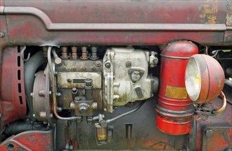 A close up of the engine of an old vintage tractor with red rusty bodywork and headlamp