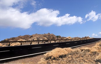 Empty two lane black road stretching to the horizon in desert scrub with blue sky and white lane