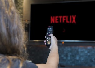 Young woman switching TV channels with remote control, Sars-CoV2 protective mask left in the corner