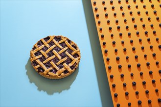 Classic blueberry pie with lattice crust on blue background and blueberries pattern on orange