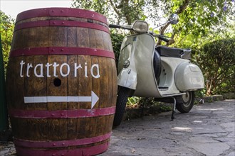 An antique wine barrel and a Vespa scooter at the entrance of a trattoria in Tuscany