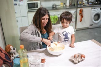 A woman and a child are making a cake together. The child is wearing a shirt that says