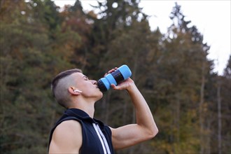 Young man drinking water from bottle while jogging in the morning outside