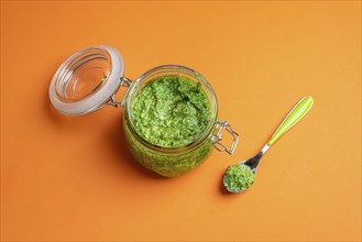 Open jar full of green pesto sauce on a seamless orange background. Homemade pesto from basil,