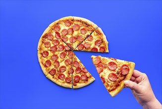 Woman's hand taking a slice of pizza, above view. Delicious pepperoni pizza isolated on a blue