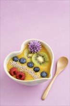 Peach smoothie bowl with blueberries, kiwi, white chia seeds and raspberries in a heart shaped bowl