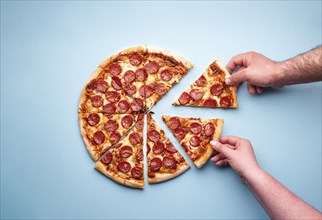 Man and woman hands grabbing pizza slices. Sliced pepperoni pizza on a blue background, above view.