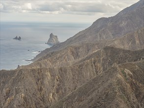 Steep cliffs and mountains along the coast with a view of the sea under a cloudy sky, tenerife,