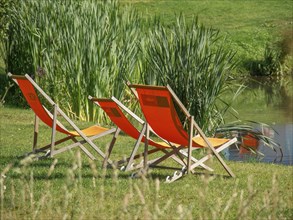 Three orange deckchairs on the banks of a pond in summer, papenburg, emsland, germany