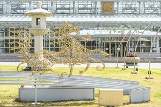 A golden sculpture of a horse next to a lantern in front of a building with a glass facade in