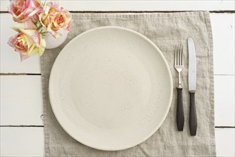 Empty cream-coloured plate with old cutlery on a linen napkin with roses