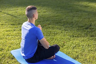 Young man wearing athletic wear sitting in the park exercising yoga