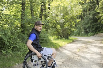 Happy and young disabled or handicapped man sitting on a wheelchair in nature turning wheels on a