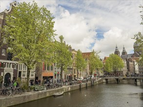 Cheerful street view with a canal, bridge and classical buildings surrounded by green trees,