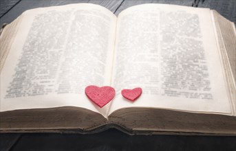 Two red hearts on the pages of an old open book, displayed on a vintage black table. A concept for