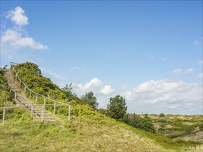 Wooden staircase winds up a green hill under a slightly cloudy sky, spiekeroog, east frisia, north