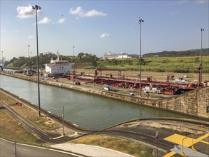 Scene in an industrial area with a large ship in the canal surrounded by containers and buildings.