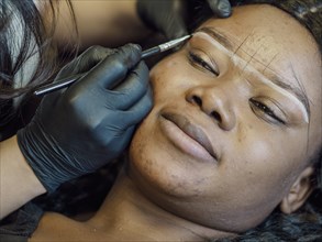 A person is lying down while having their eyebrows shaped using a makeup brush