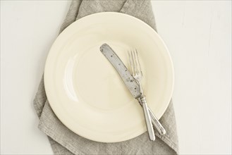 Empty cream-coloured plate with old cutlery on a linen napkin