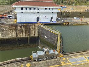 Lock with a locomotive on rails in front of a building. The canal is calm and the sky is clear,