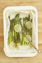 Baked green asparagus with lemon slices with baking paper in a baking dish