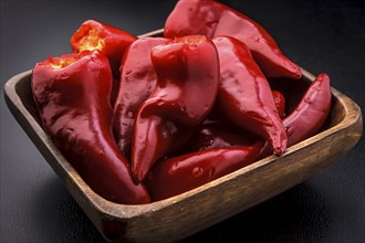 A close up of a wooden bowl full of bright red chili peppers