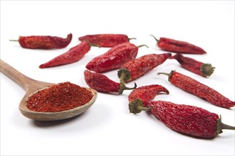 A close up still life photo of red pepper powder in a wooden spoon next to partially dried red