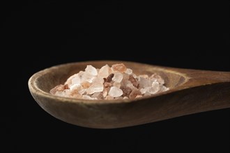 A close up photo of coarse himalayan sea salt on a wooden spoon against a black background