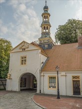 Historic building complex with archway entrance and a high church tower, with cobblestone path and